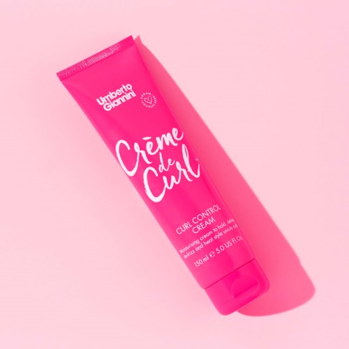 Bright pink tube labeled 'Creme de Curl' with a shadow on a pink background.