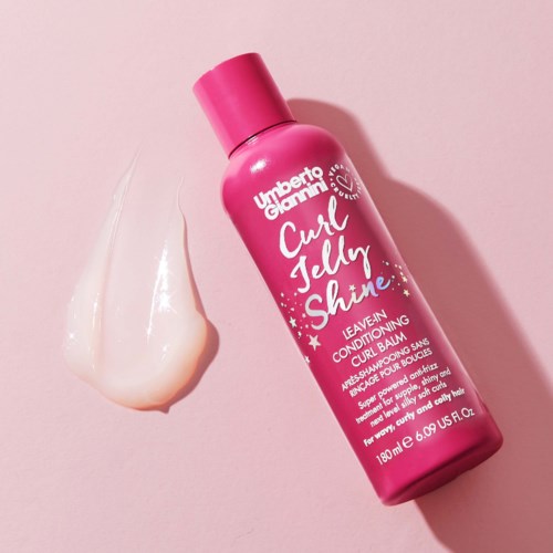 Pinkki pullo Umberto Giannini Curl Jelly Shine -läähdytystä ja pieni määrä geeliä vierellä vaaleanpunaisella taustalla.