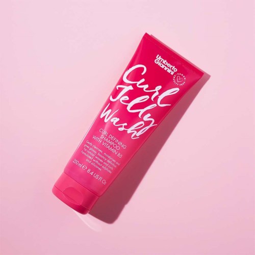 Eine pinke Tube mit Locken definierender Creme mit Vitamin B5, genannt Carol Jelly Wash, liegt auf rosa Hintergrund.