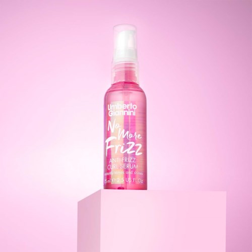 RoteSprühflasche mit der Aufschrift 'No More Frizz' auf hellem rosa Hintergrund.