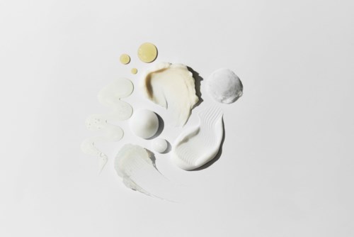 Verschillende witte en gele crèmes en lotions verspreid op een witte ondergrond.