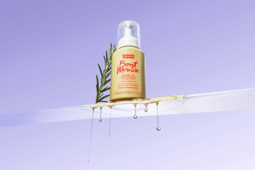 A yellow bottle labeled 'Beauty Boost Mousse' with a sprig of rosemary and honey dripping from it on a clear surface.