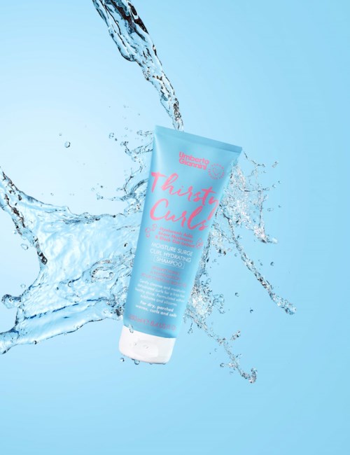 Een blauwe tube shampoo spat met water op een lichtblauwe achtergrond.