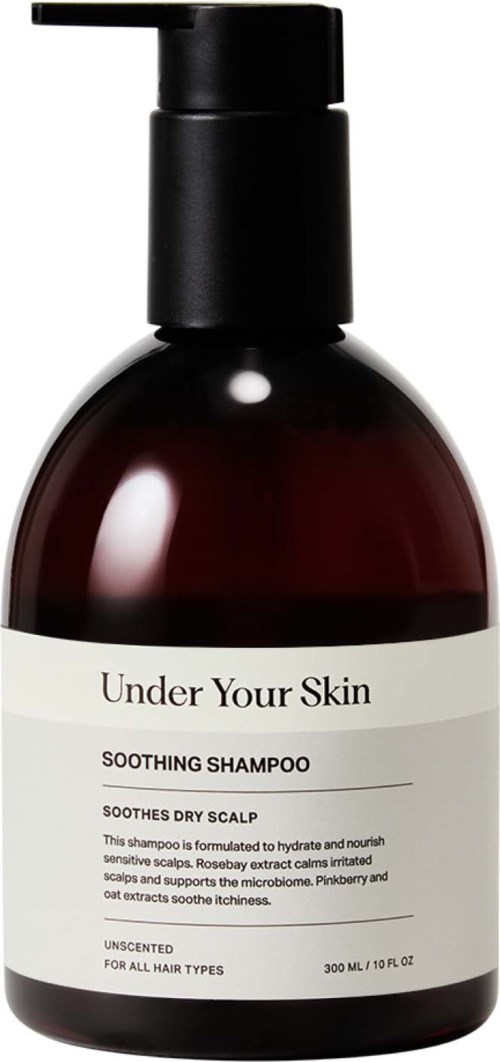 Donkerrode shampoo fles met zwarte pomp, gelabeld "Under Your Skin" verzachtende shampoo voor droge hoofdhuid.