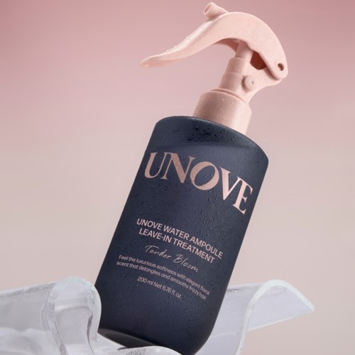 Een donkerblauwe fles met een roze spraydop, labeled UNOVE waterampool leave-in behandeling, op een witte gebogen ondergrond.