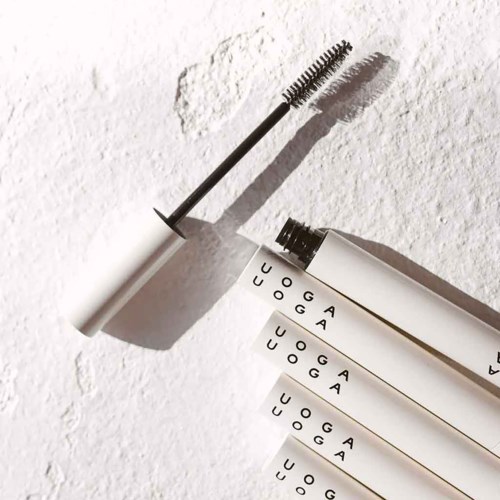 Ein Mascara-Bürste mit schwarzer und weißer Tube, wirft Schatten auf eine strukturierte weiße Oberfläche.