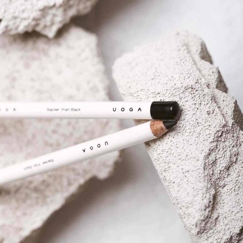 Zwei weiße Make-up-Pinsel mit schwarzen und braunen Spitzen ruhen auf rauen grauen Steinen.