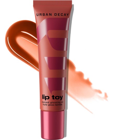 Urban Decay läppglansrör med rosa lock, smuddat persikofärgad läppstift och en persikofärgad fläck bakom.