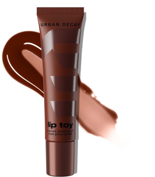 Läppglanstub med Urban Decay-logga och brunt skuggning, med en glansprovtavla bakom.