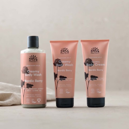 Three skincare products with pink labels and black caps: body wash, body cream, and body scrub.