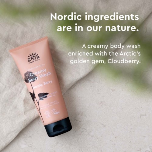 Een roze douchegels genaamd 'Creamy Body Wash' met afbeeldingen van zwarte en witte bessen, op zacht stof.