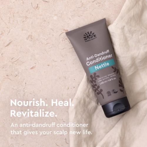Een grijze fles anti-dandruff conditioner met blauwe label en zwart bloemontwerp, geplaatst op een lichte ondergrond.