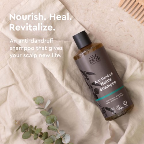 Een bruine fles anti-roosshampoo op een doek, met een plantentak ernaast. Tekst promoot voedende shampoo.
