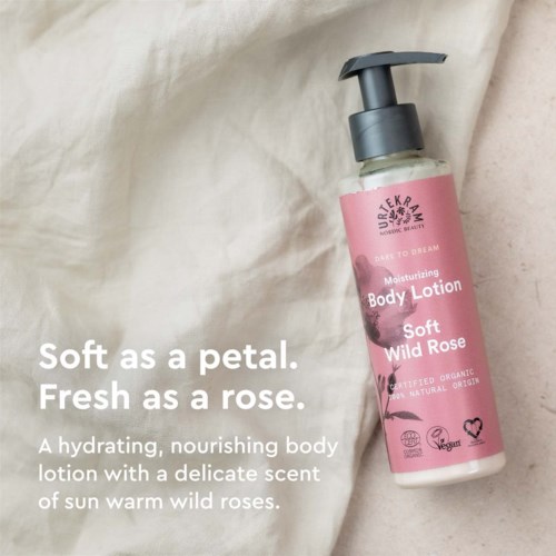 Een flesje bodylotion met roze label, zwarte pomp en witte tekst, geplaatst op lichte stofachtergrond.