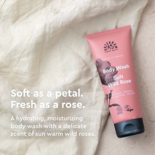 Roze lichaamswas tub met label 'Soft Wild Rose' met bloem- en bladillustraties, op een crèmekleurige stoffen achtergrond.