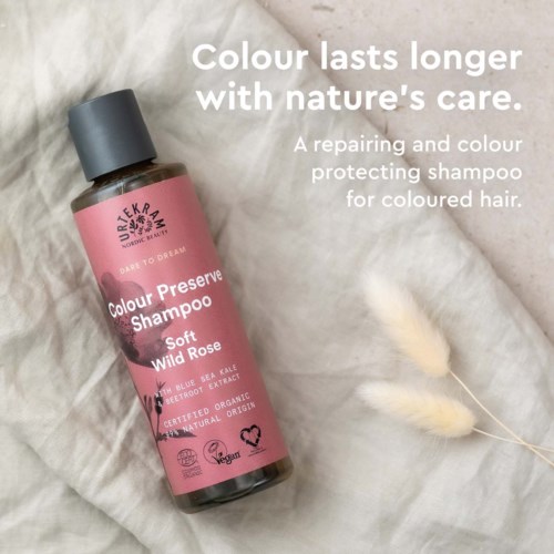 Pink shampoo bottle with black cap, laid on a white cloth with some decorations, and text promoting hair color protection.