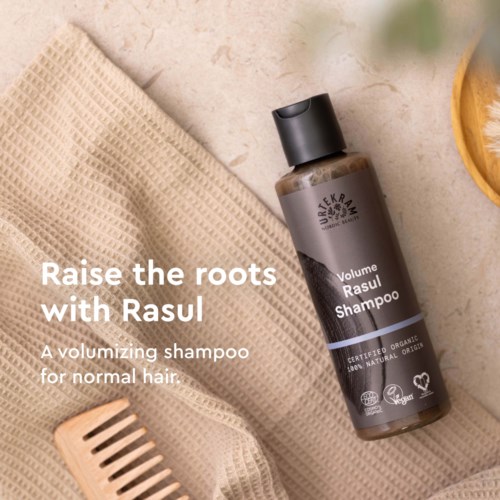 Eine Flasche Rasull Shampoo auf einem Handtuch, mit einem Kamm daneben, fördert Volumen und natürliche Schönheit.