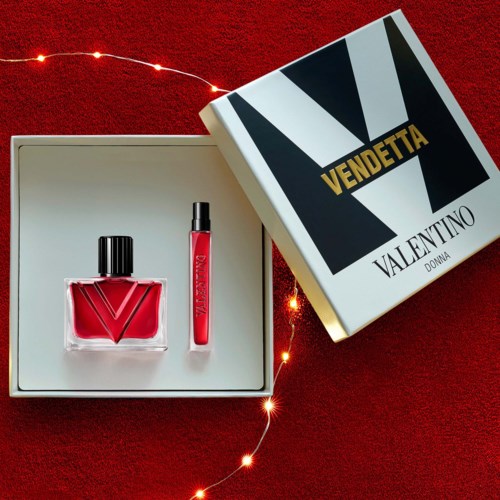 Rødt lipgloss og neglelakk i en hvit boks på en rød overflate, med en Valentino Vendetta-eske i nærheten.