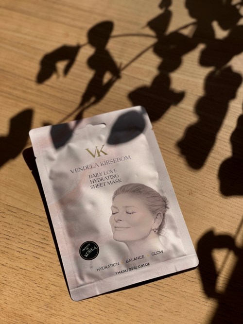 En pose med ansiktsmaske som viser en kvinne med lukkede øyne og et rolig smil, sollys og skygger på den.