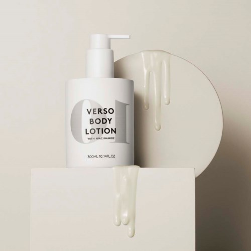 Een witte fles bodylotion met pomp, gelabeld "Verso Body Lotion," op een witte ondergrond met lotiondruppels.