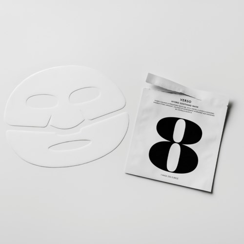 Een wit gezichtsmasker en een pakket met een zwart-wit abstract ontwerp liggen op een witte ondergrond.