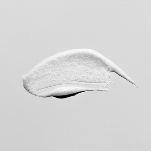 Een witte crème of lotion over een effen grijze achtergrond met een kleine punt aan het einde.