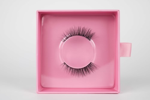 The image shows a pair of false eyelashes in a pink box. The box is open, showing the eyelashes inside.