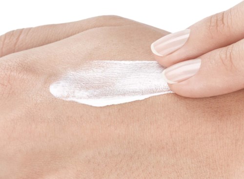 Eine Person trägt weiße Creme auf die Haut auf, Nahaufnahme zeigt Haut und Handdetails.