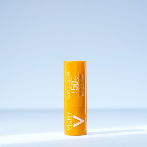 A yellow sunscreen stick with SPF 50 from Vichy, labeled 'Capital Soleil.' It stands upright on a light background.
