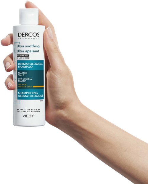 Eine Hand hält eine weiße Flasche Dercos-Shampoo, geeignet für empfindliche Kopfhaut und trockenes Haar.