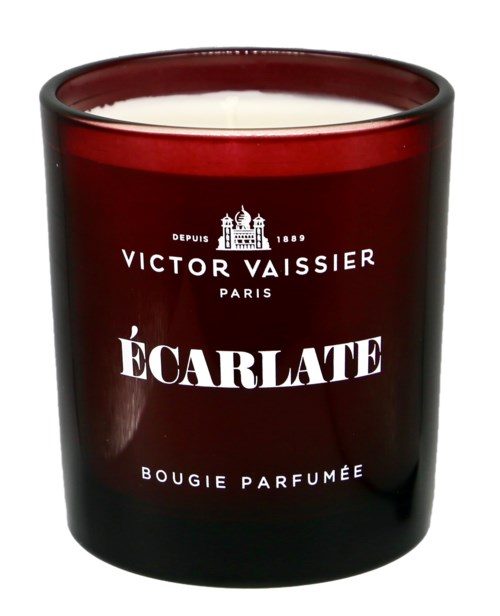 A red candle in a dark glass holder with white wax and French brand name. It is scented and decorative.