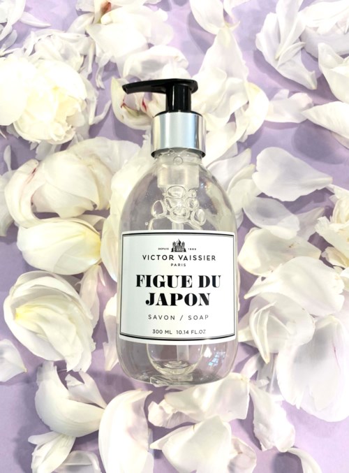 Eine klare Seifenspenderflasche mit Pumpe trägt ein Label mit der Aufschrift 'Figue du Japon' und ist mit weißen Blütenblättern bedeckt.