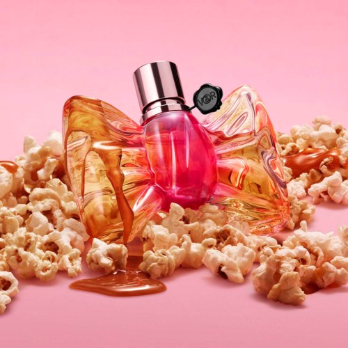 En parfymflaska omgiven av popcorn på en rosa bakgrund.