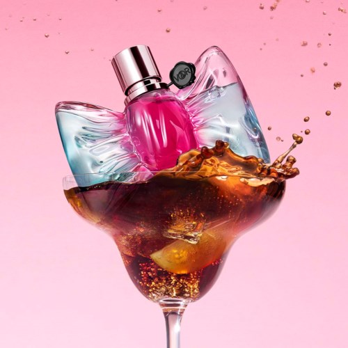 Rosa parfyllåda i glas med vätskesplash, mot rosa bakgrund, med guldglitter.