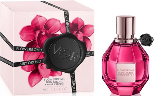 Een roze parfumfles met een glanzende dop naast een doos versierd met roze orchideeën en zwarte linten.