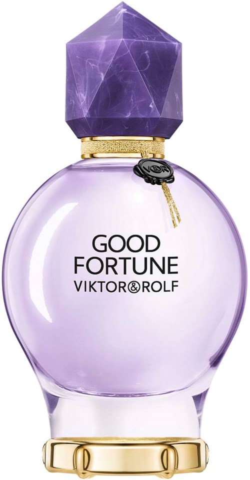 En parfymflaska med en lila ädelstens-kork och ljuslila vätska inuti. Flaskan har gulddetaljer och texten "Good Fortune".