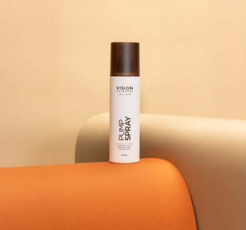 A cylindrical white and brown bottle of skincare product named 'Plump Up Spray' stands on an orange surface with a beige background.