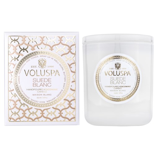 The image shows a white candle and its packaging, both labeled Voluspa Suede Blanc, with elegant gold and white designs.