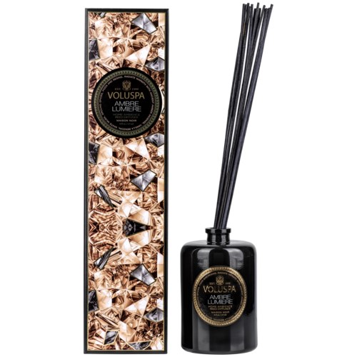 Eine schwarze Diffusorflasche und eine hohe, dekorierte Box mit goldenem Titel, enthält Reeds zum Duftverteilung.