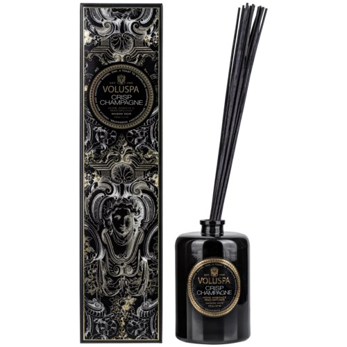 Eine schwarze Duftölspenderflasche mit langen Stäbchen und eine hohe, verzierte Verpackung mit Muster und Etikett.