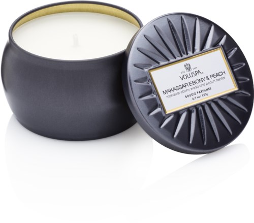 Ein schwarzer runder Kerzenglas mit Deckel, enthält weiße Wachs. Etikett sagt 'Voluspa Makassar Ebony & Peach' Duft.