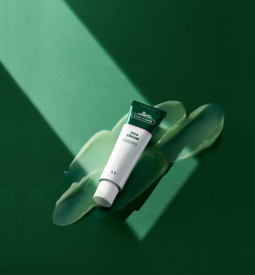Een tube Cica Cream ligt op een groene ondergrond met groene schaduw. Het label geeft aan dat het een huidverzorgingsproduct is.