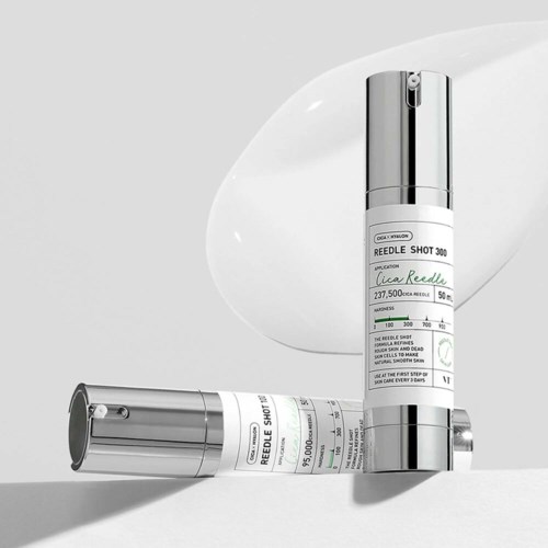 Twee metalen cosmeticaflessen met labels liggen op een witte ondergrond, met een witte crèmetekst erachter.