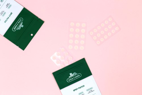 Twee groene dozen met "Spot Patch" en enkele ronde pleisters op een roze achtergrond.