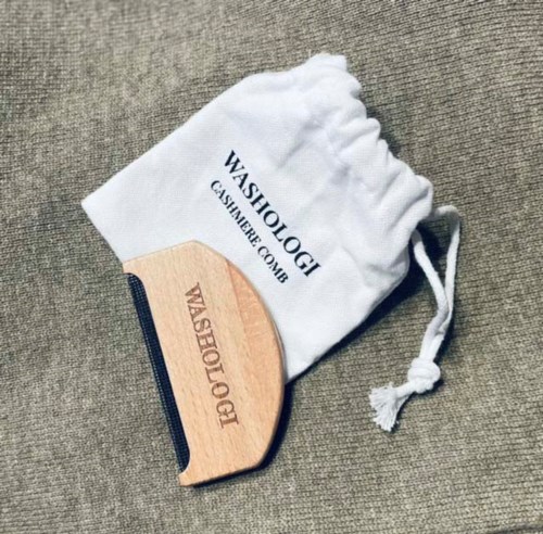 A wooden massage tool with a handle placed on a gray carpet, next to a white cloth bag. The bag has text printed on it.