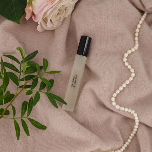A perfume bottle, a pearl necklace, pink flowers, green leaves, and a soft fabric background.