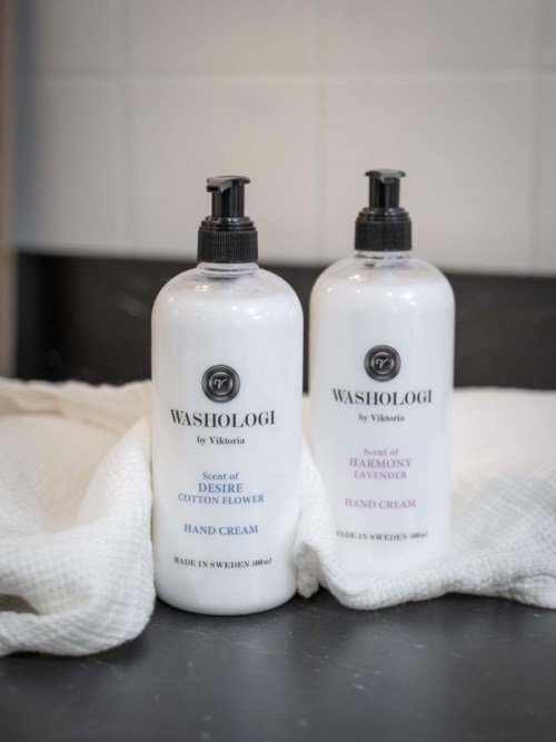 Two white hand cream bottles with black pump dispensers, placed on a white cloth surface, with a tiled background.