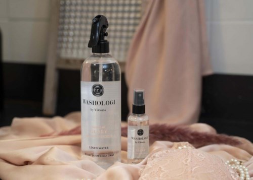 Two bottles of Washologie cleaning products on soft fabric with pearls, in a cozy setting.