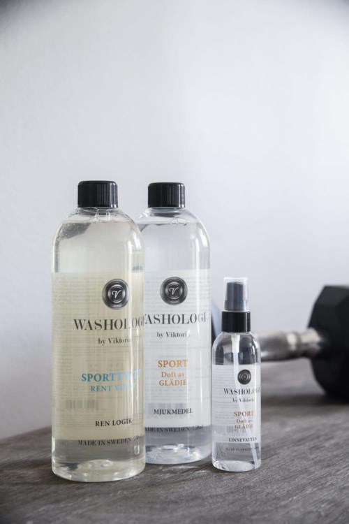 Three bottles of sports wash and a small spray bottle are on a wooden surface, next to a dumbbell.