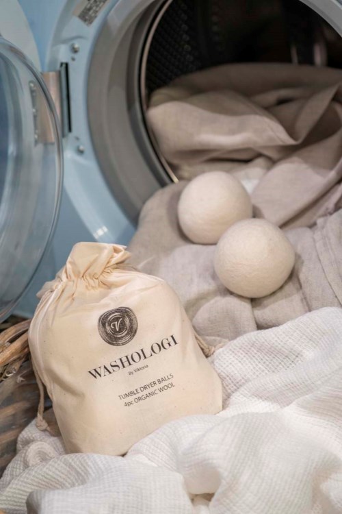 Laundry scene with two wool dryer balls and a Washologi bag in front of an open washing machine.
